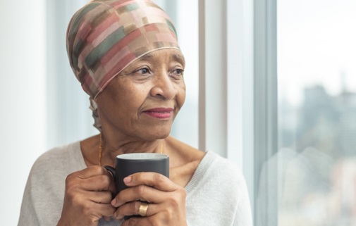 Older woman wearing a head wrap holding a cup of coffee gazing pensively out of a window