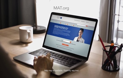 A still from the a TV ad featuring the MAT.org website, showing a person using a laptop to access the homepage of the site.