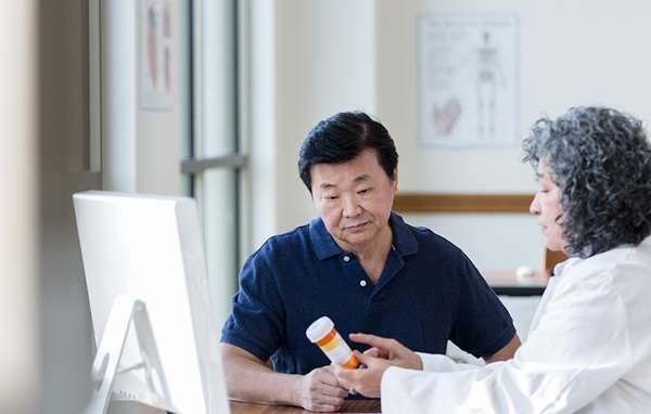 Older Asian American patient with a disheartened expression looking at a medication bottle being held by his doctor