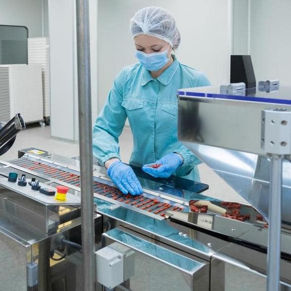 Biopharmaceutical manufacturing worker working with medication tablets on a conveyor belt