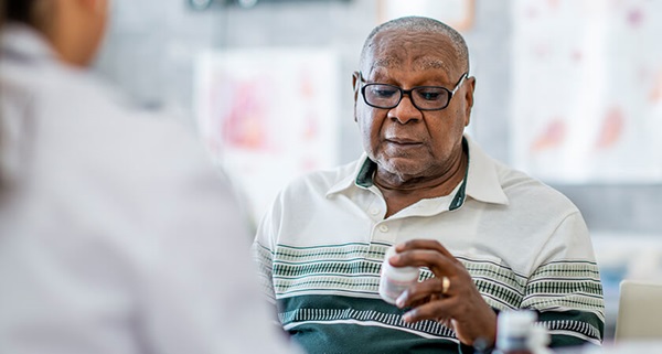 A photograph of an older african-american man reading a medication bottle with his eyebrows slightly raised in an expression of mild surprise
