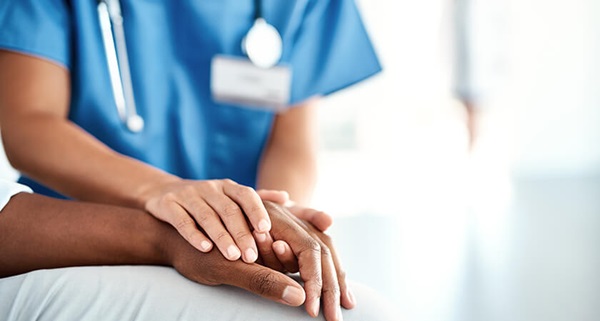 A closeup photograph of the hands of a health care provider holding another person's hand, on the top and bottom