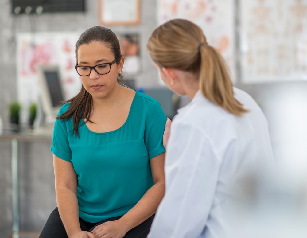 Woman with expression of nervous concern is comforted by her doctor